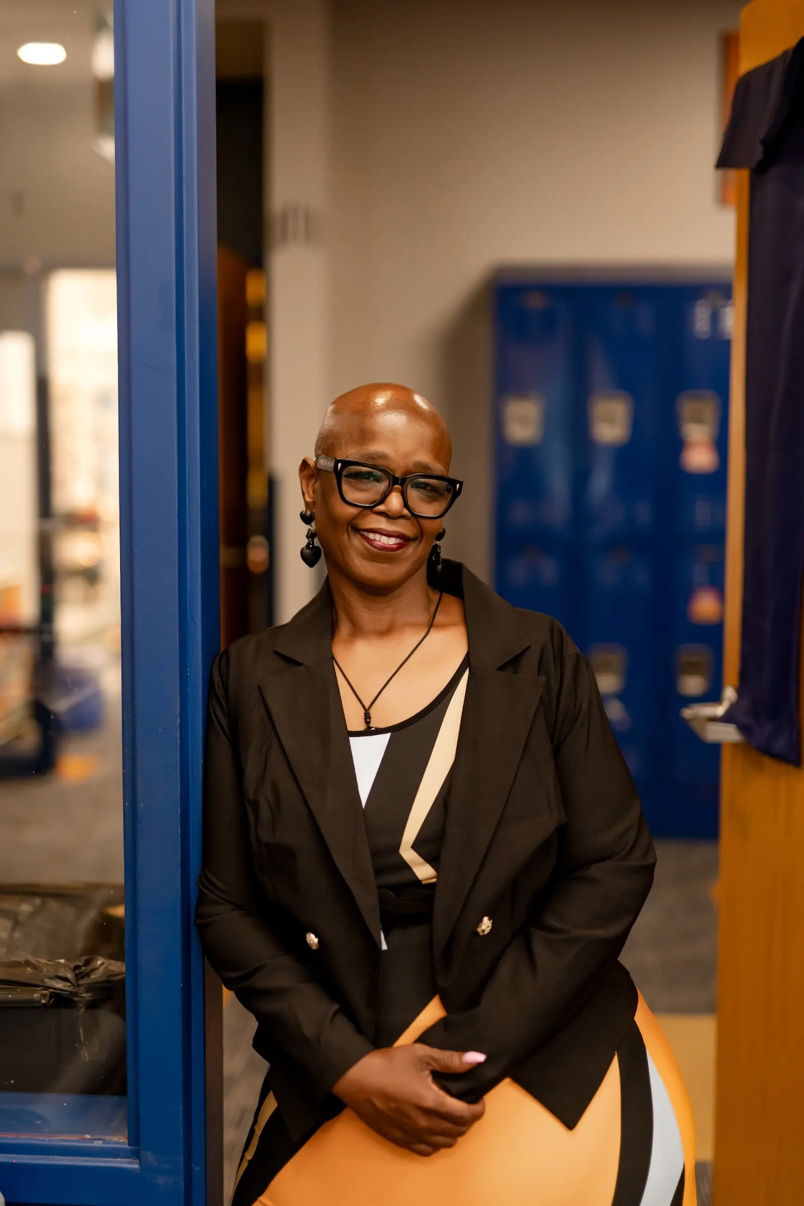 Angelia Moore smiling, seated in a school hallway in a black blazer